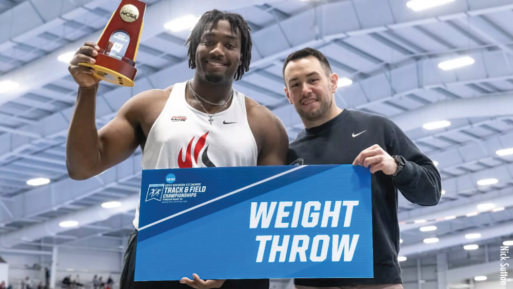 Carthage College Track & Field Athlete Joseph White and coach Greg Raimondi holding a weight throw sign at NCAA Track & Field Championships 